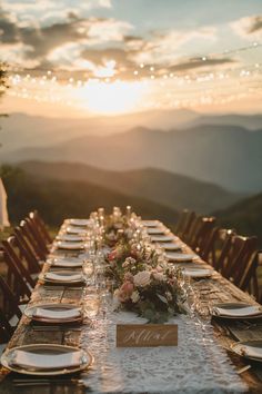 a long table with plates and place settings on it in front of the mountains at sunset