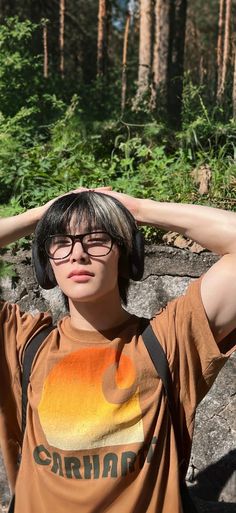 a young man wearing headphones standing in front of trees and rocks with his hands on his ears