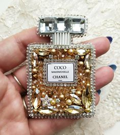 a hand holding a small square shaped perfume bottle covered in gold and silver beads with the label coco mademoiselle chanel