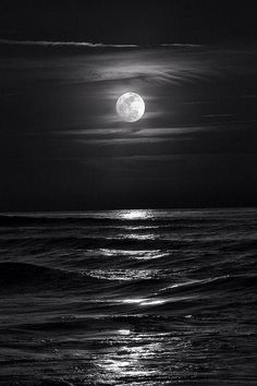 the moon is shining over the ocean with waves in front of it and dark clouds