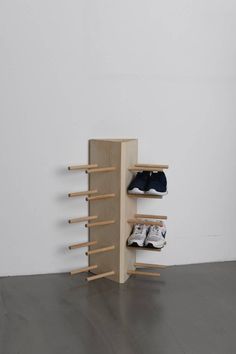 a wooden shoe rack with two pairs of shoes on it and one pair of sneakers hanging off the wall