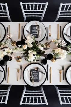 the table is set with black and white plates, silverware, gold cutlery, and floral centerpieces