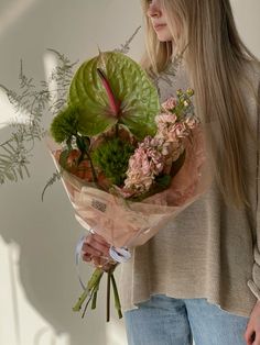 a woman holding a bouquet of flowers and greenery in front of a white wall