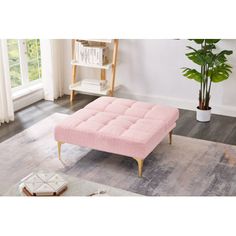 a pink couch sitting on top of a wooden floor next to a potted plant