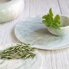 two plates with herbs on them sitting on a table next to each other, one plate has a green sprig in it