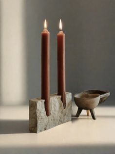 two candles sitting on top of a stone block next to a bowl