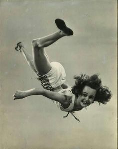 an old black and white photo of a woman in the air with her feet up