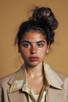 a woman wearing a beige suit and gold shirt with her hair in a top knot