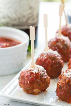 several meatballs with toothpicks in them on a white plate next to dipping sauce