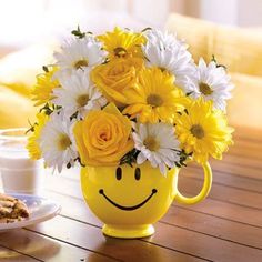 a smiley face mug filled with yellow and white flowers