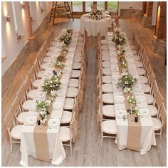 a long table set up with white linens and greenery on it for a wedding reception