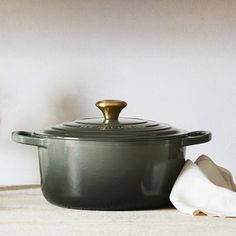 a pot with a gold lid sitting on a table next to a white towel and glass vase