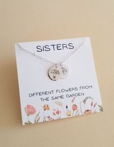 a card with a silver necklace on it that says, sisters different flowers from the same garden