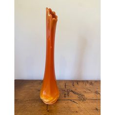 an orange glass vase sitting on top of a wooden table next to a white wall