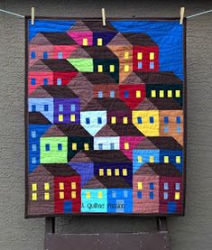 a quilt hanging on the side of a building with houses painted on it and some clothes pins