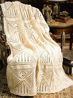 a white crocheted blanket sitting on top of a chair next to a table