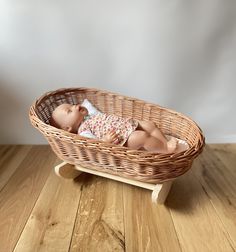 a baby doll laying in a basket on a wooden floor next to a white wall