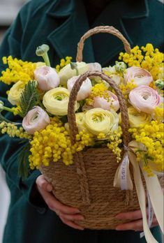 a person holding a basket with flowers in it and a ribbon around the handle,