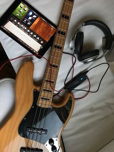 an electric guitar and headphones are laying on a bed next to a tablet computer