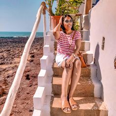 a woman is sitting on the steps by the beach and talking on her cell phone