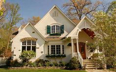 a white house with green shutters on the front and side windows, surrounded by trees