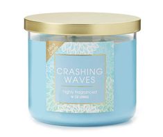 a blue candle with gold lid and the words crashing waves on it's front