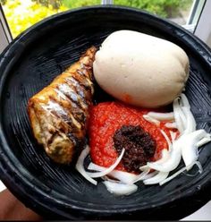 a black plate with meat, onions and tomato sauce on it in front of a window