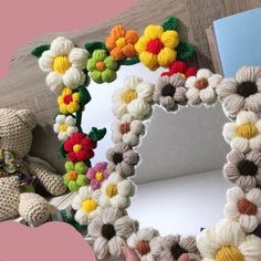 there is a crocheted flower frame with a teddy bear in front of it