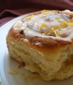 a white plate topped with a pastry covered in icing and lemon zests