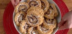 a bowl filled with cookies on top of a red place mat next to two hands