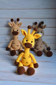 three stuffed giraffes sitting next to each other on a wooden floor with white boards behind them