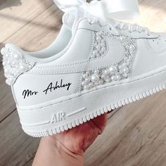 a person holding up a white nike air force with pearls on the side and an embroidered name