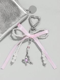 a silver purse with pearls and a pink ribbon tied around the strap, next to it is a heart shaped keychain