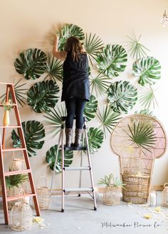 a woman standing on top of a ladder in front of a wall with monster leaves