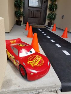 a red car is parked in front of orange cones on the side of a house