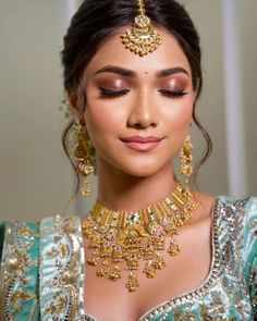 a woman in a blue dress with gold jewelry on her neck and chest, looking down at the camera