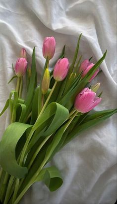 a bouquet of pink tulips sitting on top of a white bed sheet with green stems