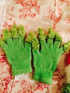 two green gloves sitting on top of a bed next to a teddy bear and christmas tree