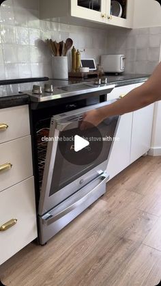 a person is opening the oven door in a kitchen with white cabinets and wood flooring