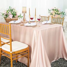 the table is set with two gold chairs and one pink tablecloth has flowers in vases on it