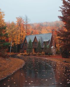 a large house surrounded by trees in the fall with leaves on the ground and wet pavement