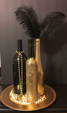 three vases with pearls and beads are on a gold plate next to two black bottles