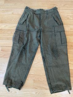 These thick warm wool vintage German military pants  are so well made that, though they are showing some wear, they have lots of life left in them. There is thick stitching everywhere, buttons (with lined flaps!)  to secure all the pockets, and ties at the bottom of each leg to tighten it or button it up shorter as needed. They are high-waisted with a button fly and a double button front closure (one of the buttons is missing). Each side of the waistband has a button adjustment to tighten the wa Vintage Cargo Pants With Pockets For Fall, Vintage Fall Cargo Pants With Pockets, Winter Military Bottoms With Side Pockets, Vintage Winter Bottoms With Pockets, Retro Style Winter Workwear Pants, Vintage Full Length Bottoms For Winter, Vintage Tapered Leg Winter Pants, Vintage Wide Leg Pants For Winter, Vintage Full-length Winter Pants