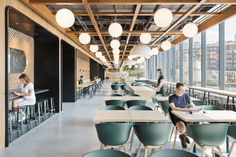 people are sitting at tables in an open area with lots of windows and green chairs