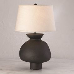 a black table lamp with a white shade on the base and a beige linen lampshade