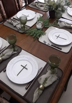 the table is set with white plates, silverware and greenery on top of them