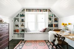 a room with a window seat, desk and bookshelf in the corner next to it