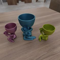 three different colored cups sitting on top of a wooden table next to each other,