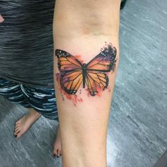 a woman's arm with a watercolor tattoo of a butterfly on the left forearm