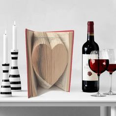 two wine glasses and an open book on a table next to candle holders with books